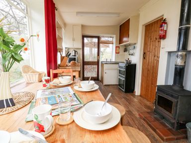 A kitchen with a wooden table set with bowls cups and a magazine near a window with a wood burning stove at Eweleaze in West Bexington