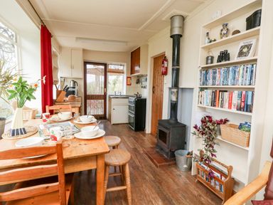 A kitchen with a wooden dining table set with bowls and mugs a stove and wood burning stove and a bookshelf with books and DVDs at Eweleaze in West Bexington