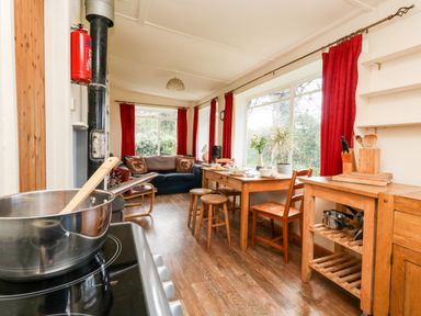 A kitchen and dining area with wooden furniture red curtains and a sofa at Eweleaze in West Bexington