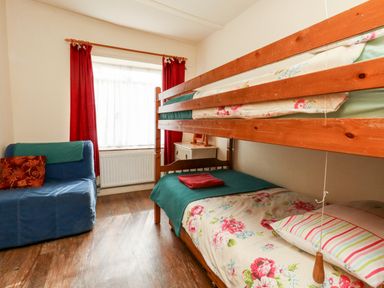 A bedroom with wooden bunk beds a blue armchair red curtains and a small cabinet at Eweleaze in West Bexington