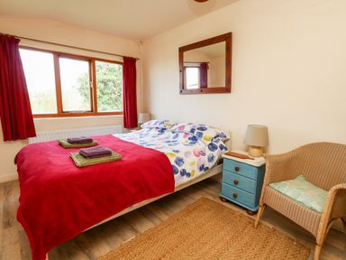 A bedroom with a double bed red blanket bedside table lamp and wicker chair at Eweleaze in West Bexington