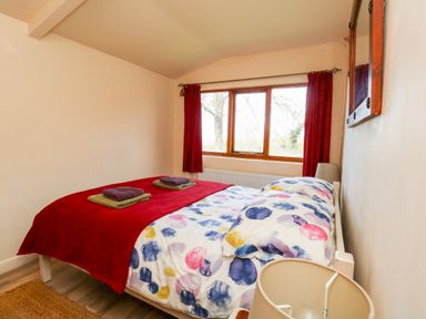 A bedroom with a double bed covered with a colorful duvet and red blanket near a window with red curtains at Eweleaze West Bexington