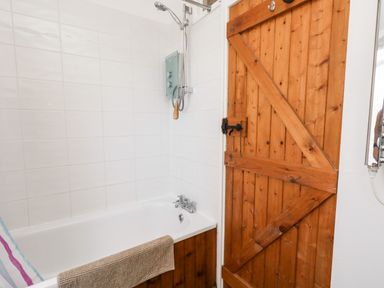 A bathroom with a bathtub shower and wooden door at Eweleaze in West Bexington
