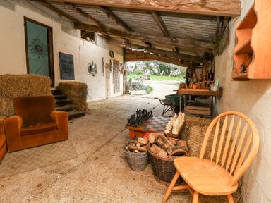 A rustic covered outdoor area with a wooden chair a chessboard a leather armchair and baskets of firewood at Eweleaze in West Bexington