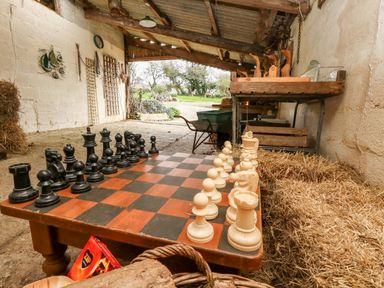 A large chessboard with pieces set up on a table in a rustic barn with hay and gardening tools at Eweleaze in West Bexington