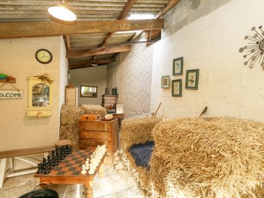 A rustic room with hay bales used as furniture a wooden chest a chessboard on a table and framed pictures on the wall at Eweleaze in West Bexington