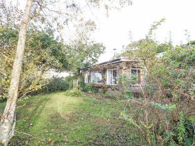 A stone house with large windows surrounded by trees and grass at Eweleaze in West Bexington