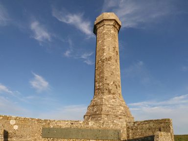 A tall stone monument with a plaque on a low stone wall under a blue sky at Eweleaze in West Bexington