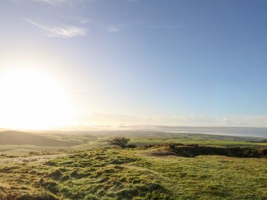 A grassy hill overlooking fields and a distant body of water under a clear sky at Eweleaze in West Bexington