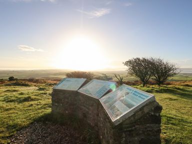 Information boards on a stone stand with grassy fields and trees under a clear sky at Eweleaze in West Bexington