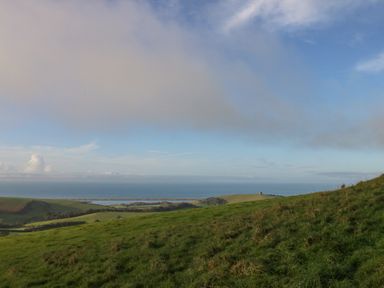 A grassy hillside overlooking fields and the sea under a partly cloudy sky at Eweleaze in West Bexington