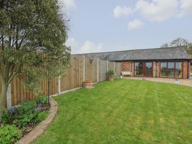 A garden with a tree lawn plants flower pots and a brick building with large windows at Bee Happy Barn in Beighton near Acle