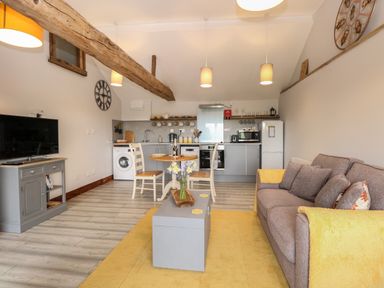 An open plan living area with a sofa a coffee table a dining table and chairs a kitchen with appliances and exposed wooden beams at Bee Happy Barn in Beighton near Acle