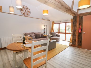 A living room with a wooden dining table set for two and a seating area with a sofa and armchair at Bee Happy Barn in Beighton near Acle