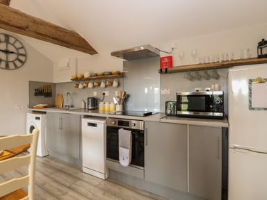 A kitchen with grey cabinets white appliances wooden shelves and a large wall clock at Bee Happy Barn in Beighton near Acle