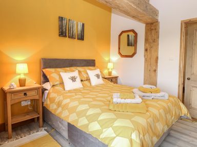 A bedroom with a double bed matching yellow bedding and pillows with bees on them two bedside tables with lamps and folded towels on the bed at Bee Happy Barn in Beighton near Acle