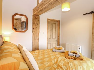 A bedroom with a patterned bedspread pillows stacked towels a wooden door and octagonal wall mirror at Bee Happy Barn in Beighton near Acle