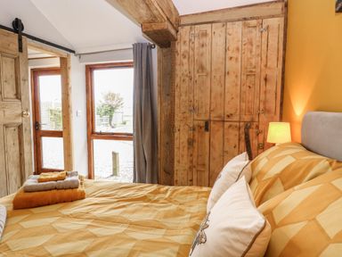 A bedroom with a bed covered in yellow bedding and pillows beside a wooden wardrobe and door at Bee Happy Barn Beighton near Acle