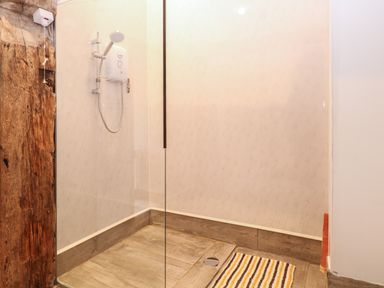 A walk in shower with a wooden effect floor and a striped bath mat at Bee Happy Barn in Beighton near Acle