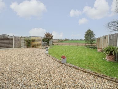 A backyard with gravel area and grass lawn separated by a stone border with potted plants at Bee Happy Barn in Beighton near Acle