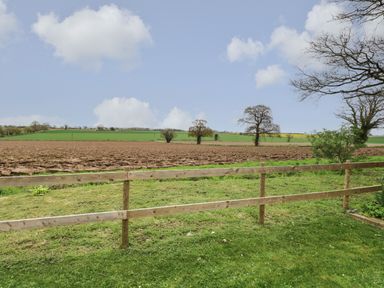 A rural landscape with green grass a wooden fence plowed field distant trees and a blue sky at Bee Happy Barn in Beighton near Acle