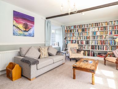 A living room with a gray sofa a wooden coffee table a bookshelf filled with books and an armchair at West Farm Cottage in Longhorsley