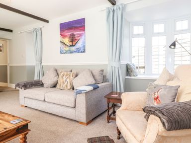A living room with a grey sofa a beige armchair a wooden coffee table a side table and a window with curtains at West Farm Cottage in Longhorsley