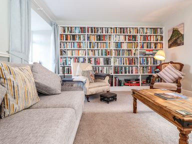 A living room with a large bookshelf sofa armchairs and a wooden coffee table at West Farm Cottage in Longhorsley