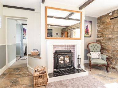 A room with a fireplace a green armchair and a wicker basket with firewood at West Farm Cottage in Longhorsley