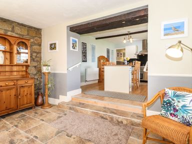 An open living space with a wooden cabinet stone wall wicker chair with cushion and kitchen area at West Farm Cottage in Longhorsley