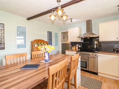 A kitchen with wooden table and chairs a vase of flowers on the table white cabinets and stainless steel oven at West Farm Cottage in Longhorsley