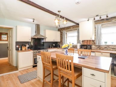 A kitchen with wooden chairs around an island and cabinets along the walls at West Farm Cottage in Longhorsley