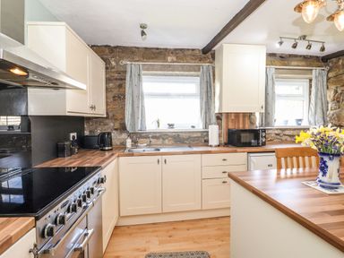 A kitchen with wooden countertops white cabinets a stove microwave kettle and flowers in a vase at West Farm Cottage in Longhorsley