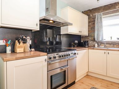 A kitchen with cream cabinets a wooden countertop a stainless steel oven a black electric kettle and a window with a curtain at West Farm Cottage in Longhorsley