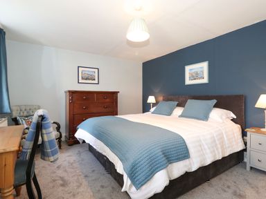 A bedroom with a large bed with blue bedding a wooden dresser a desk with a chair and two bedside tables at West Farm Cottage in Longhorsley