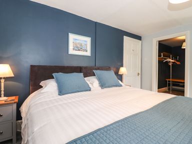 A bedroom with a double bed blue pillows and blanket bedside tables with lamps and an open walk in closet at West Farm Cottage in Longhorsley