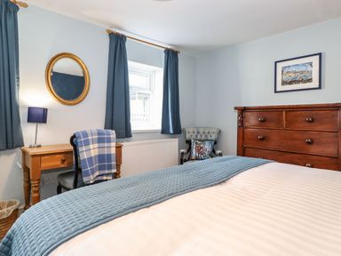 A bedroom with a wooden desk and chair a window with blue curtains a wooden dresser and an armchair at West Farm Cottage in Longhorsley
