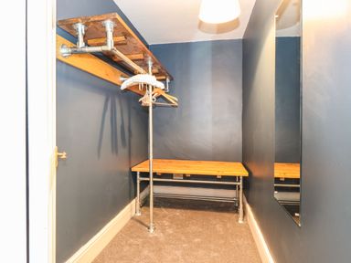 A small room with a wooden bench and shelves with metal pipes and hangers on the wall at West Farm Cottage in Longhorsley