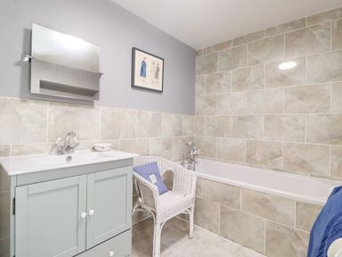 A bathroom with a sink cabinet mirror wicker chair with cushion and bathtub at West Farm Cottage in Longhorsley