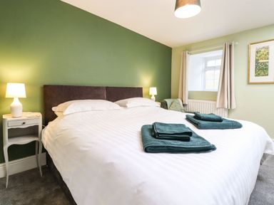 A bedroom with a large bed with white bedding and green towels on it two bedside tables with lamps and a window at West Farm Cottage in Longhorsley