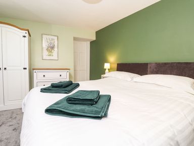 A bedroom with a bed covered in white linens and folded green towels a wardrobe and chest of drawers against the wall West Farm Cottage Longhorsley