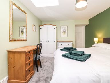 A bedroom with a wooden desk, chair, white wardrobe, white dresser, bed with green towels, and a lamp at West Farm Cottage in Longhorsley