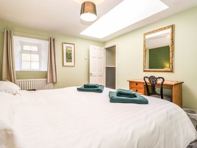 A bedroom with a bed folded towels a desk and chair a window and a mirror at West Farm Cottage in Longhorsley