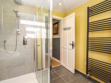A shower area with glass doors and a black towel radiator next to a door with a washroom sign at West Farm Cottage in Longhorsley