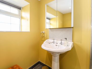 A bathroom with a white pedestal sink a mirror cabinet and a window at West Farm Cottage in Longhorsley