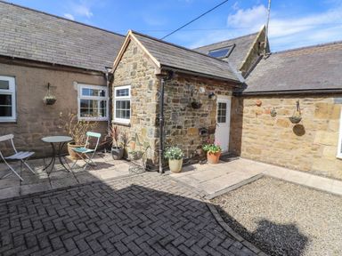 A stone courtyard with potted plants two chairs and a small table at West Farm Cottage in Longhorsley