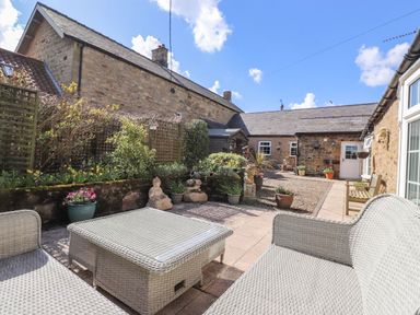 An outdoor patio area with wicker furniture stone walls plants and garden ornaments at West Farm Cottage in Longhorsley