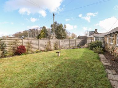 An enclosed garden with grass lawn stone birdbath wooden fencing and stone building at West Farm Cottage in Longhorsley