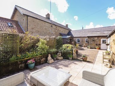 A patio with outdoor furniture stone statues potted plants and a garden area at West Farm Cottage in Longhorsley