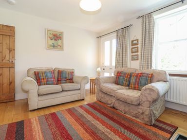 A living room with two sofas with plaid cushions a striped rug wooden door and window with curtains at High Stile in Seatoller near Rosthwaite
